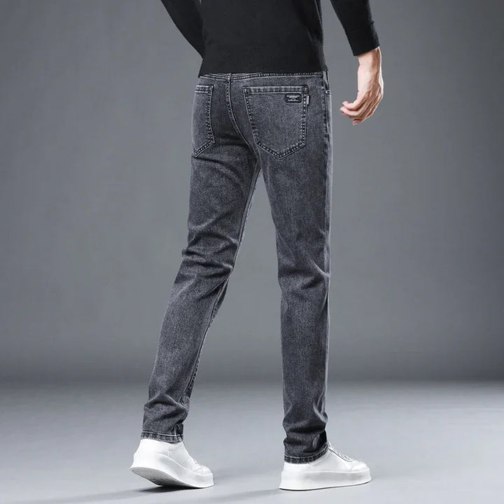 Back view of man wearing slim fit grey jeans with white sneakers on gray background