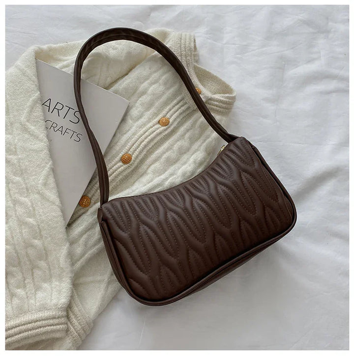 Brown quilted leather shoulder bag on cream knit sweater with orange buttons and arts crafts book