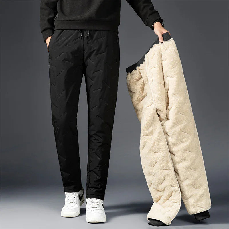 Man wearing black insulated pants and holding beige fleece-lined winter pants against gray background