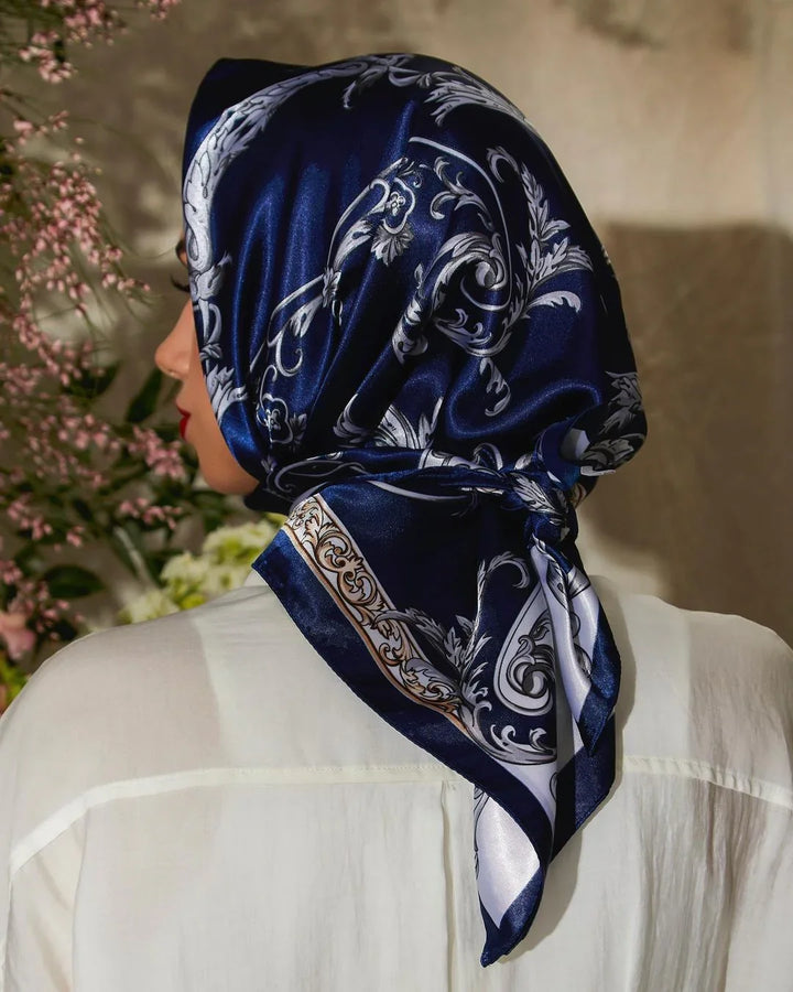 Woman wearing a navy blue silk scarf with silver floral patterns over white shirt indoors