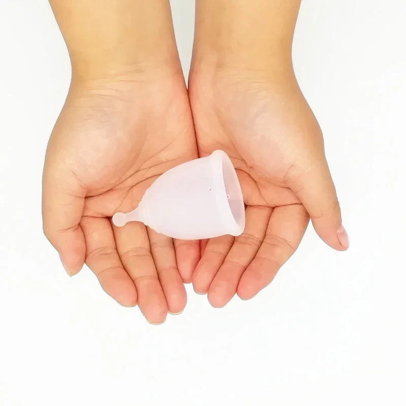 Hands holding a translucent silicone menstrual cup on white background