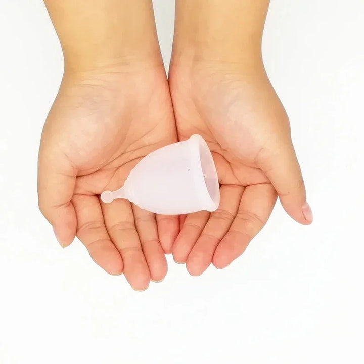 Hands holding a translucent silicone menstrual cup on white background