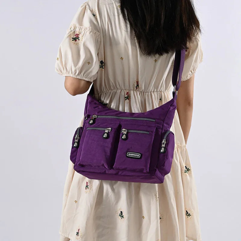 Woman wearing cream dress with floral embroidery carrying purple multi-pocket nylon shoulder bag