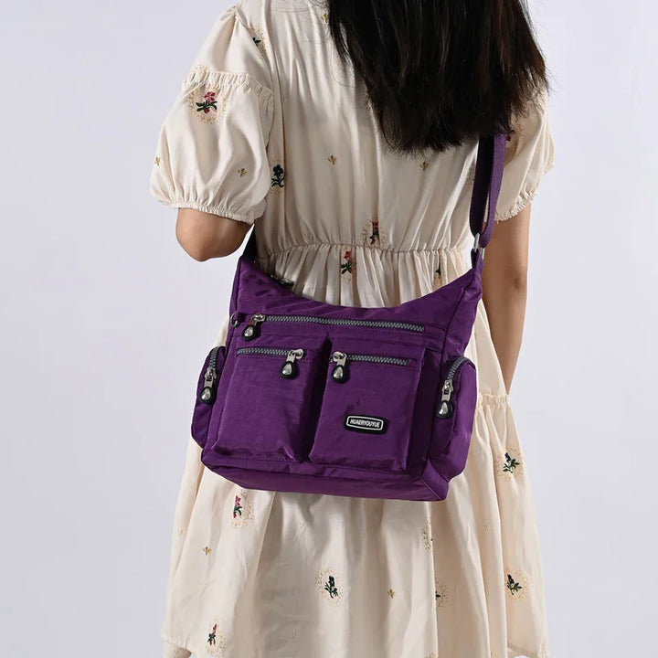 Woman wearing cream dress with floral embroidery carrying purple multi-pocket nylon shoulder bag