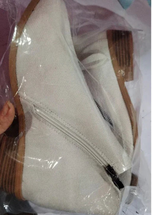 Pair of beige suede ankle boots with wooden block heels inside clear plastic packaging