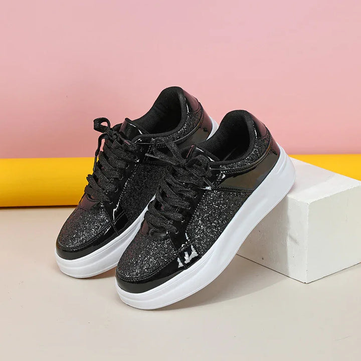 Black glittery platform sneakers with white soles against pink and yellow background