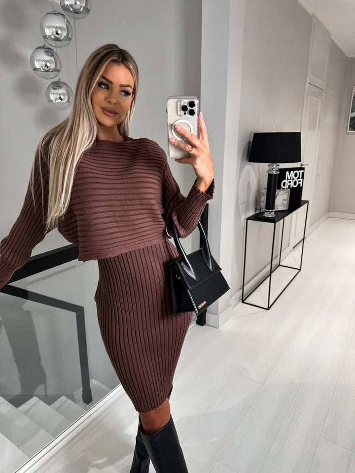 Woman in brown ribbed knit dress and black boots taking a mirror selfie in modern minimalistic room