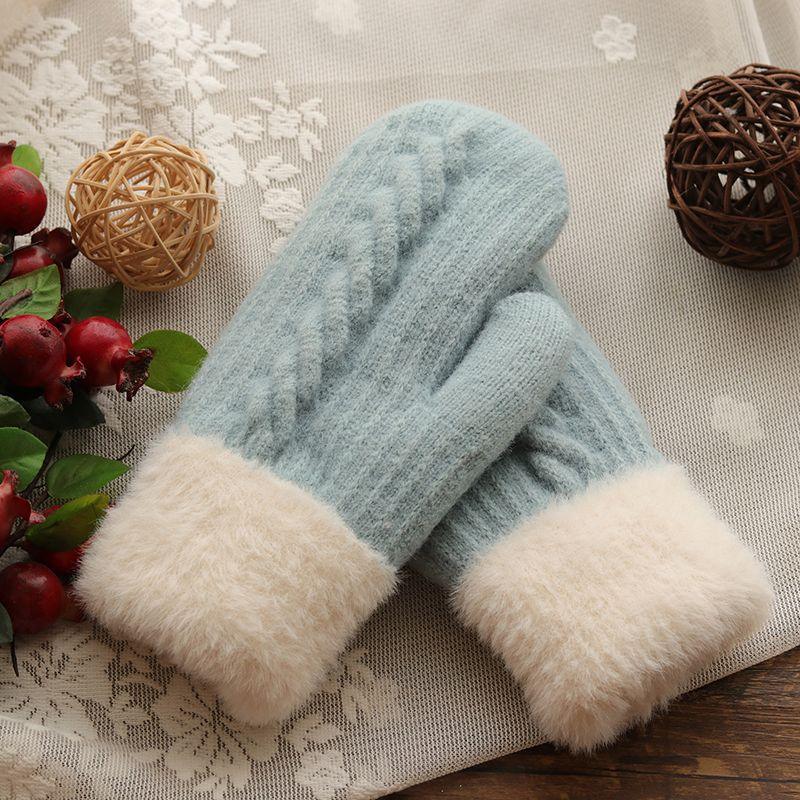 Soft gray wool mittens with cream faux fur cuffs on lace tablecloth with decorative wicker balls and red berries