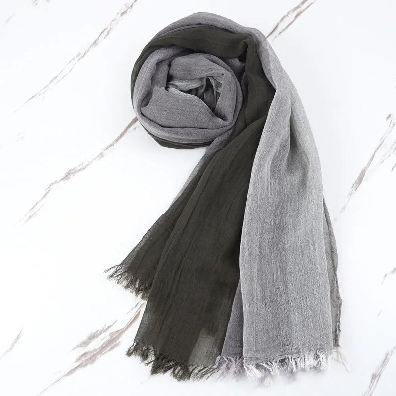 Two-tone lightweight scarf in gray and dark green with frayed edges on marble surface