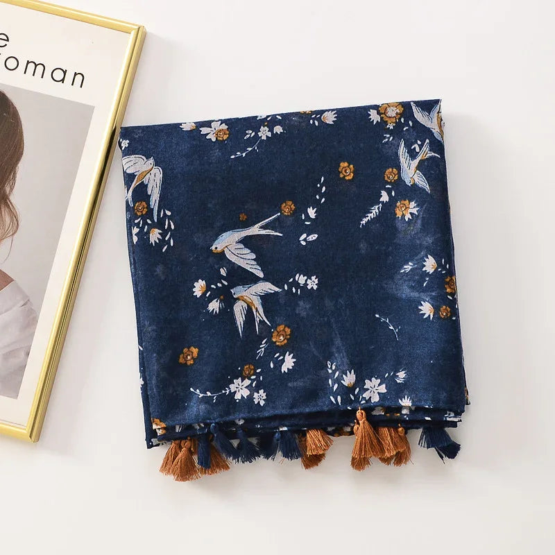 navy blue scarf with bird and floral print and brown tassels on white surface next to a framed photo