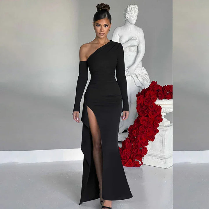 woman in elegant one-shoulder black evening gown with thigh-high slit posing indoors near white statue and red roses