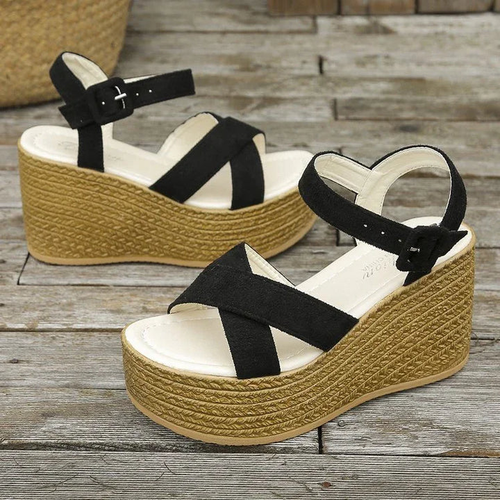Black suede crisscross strap wedge sandals with braided jute platform heels on wooden floor