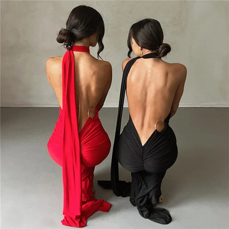 Two women kneeling in backless halter dresses, one red and one black, with low ruched skirts and gold ring details