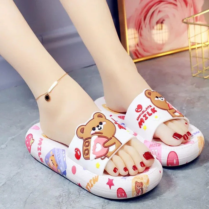 Feet wearing white slippers with cute teddy bear and chocolate milk designs on gray floor