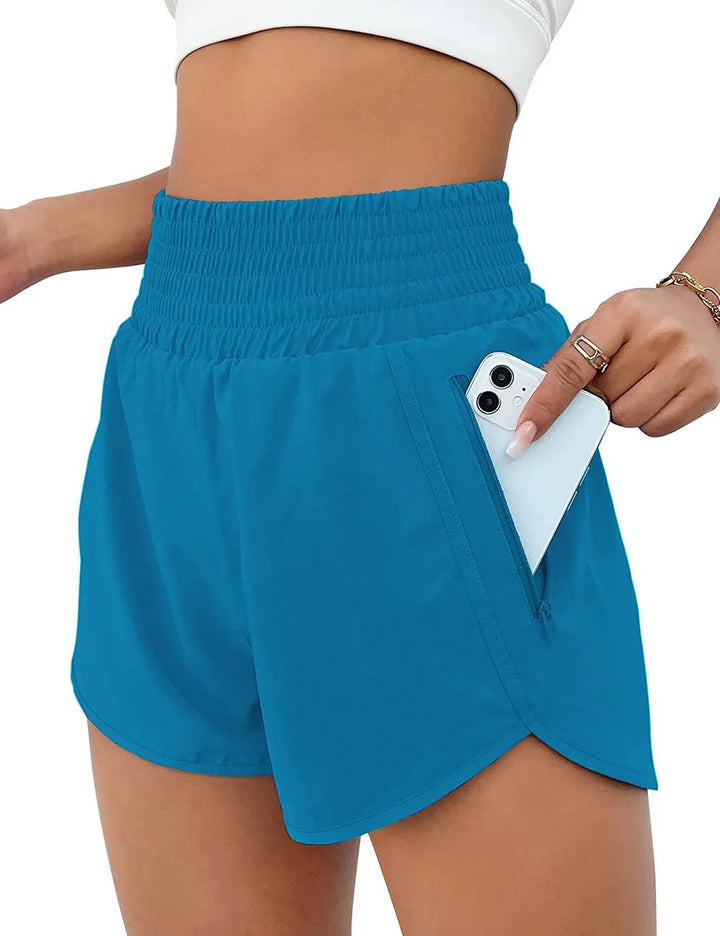 Woman wearing blue high-waisted athletic shorts with zippered pocket holding a white smartphone