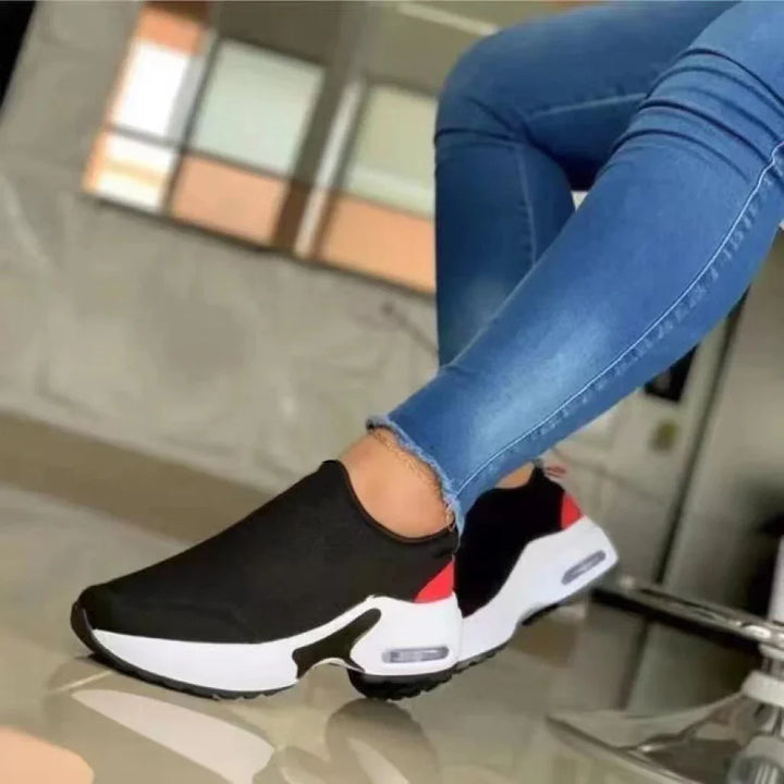 Person wearing black slip-on sneakers with white and red sole, paired with blue skinny jeans