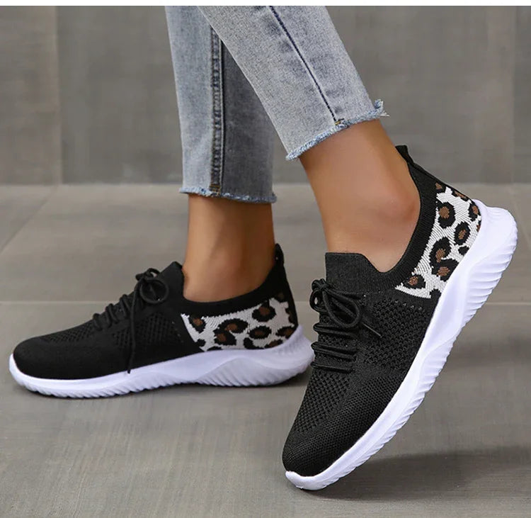 Black knitted sneakers with white soles and leopard print heel detail worn with light blue cropped jeans on gray floor