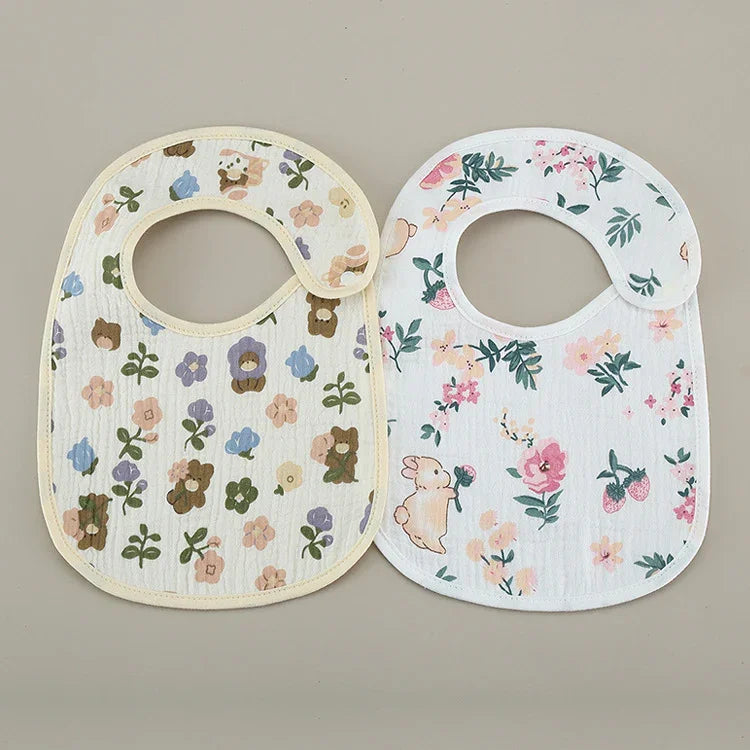 Two baby bibs with colorful floral and animal prints on a neutral background