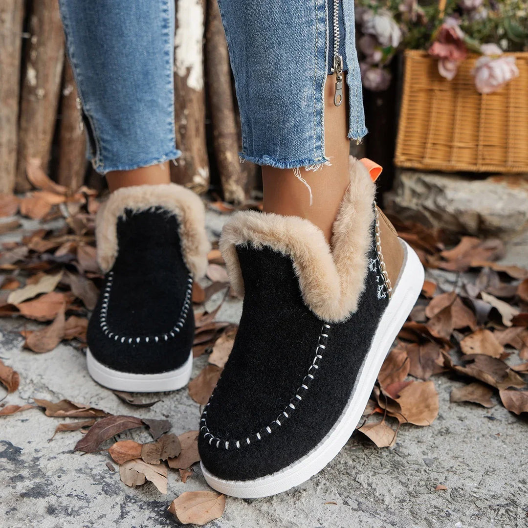 Black winter moccasin boots with fur lining worn with cropped blue jeans on a leaf-covered ground