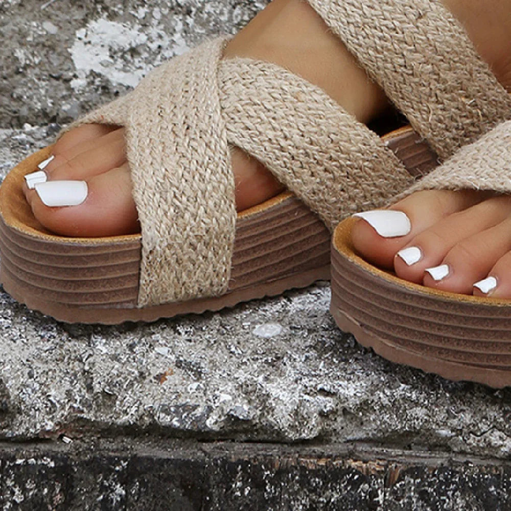 Close-up of feet with white toe nail polish wearing beige woven platform sandals on rough concrete surface