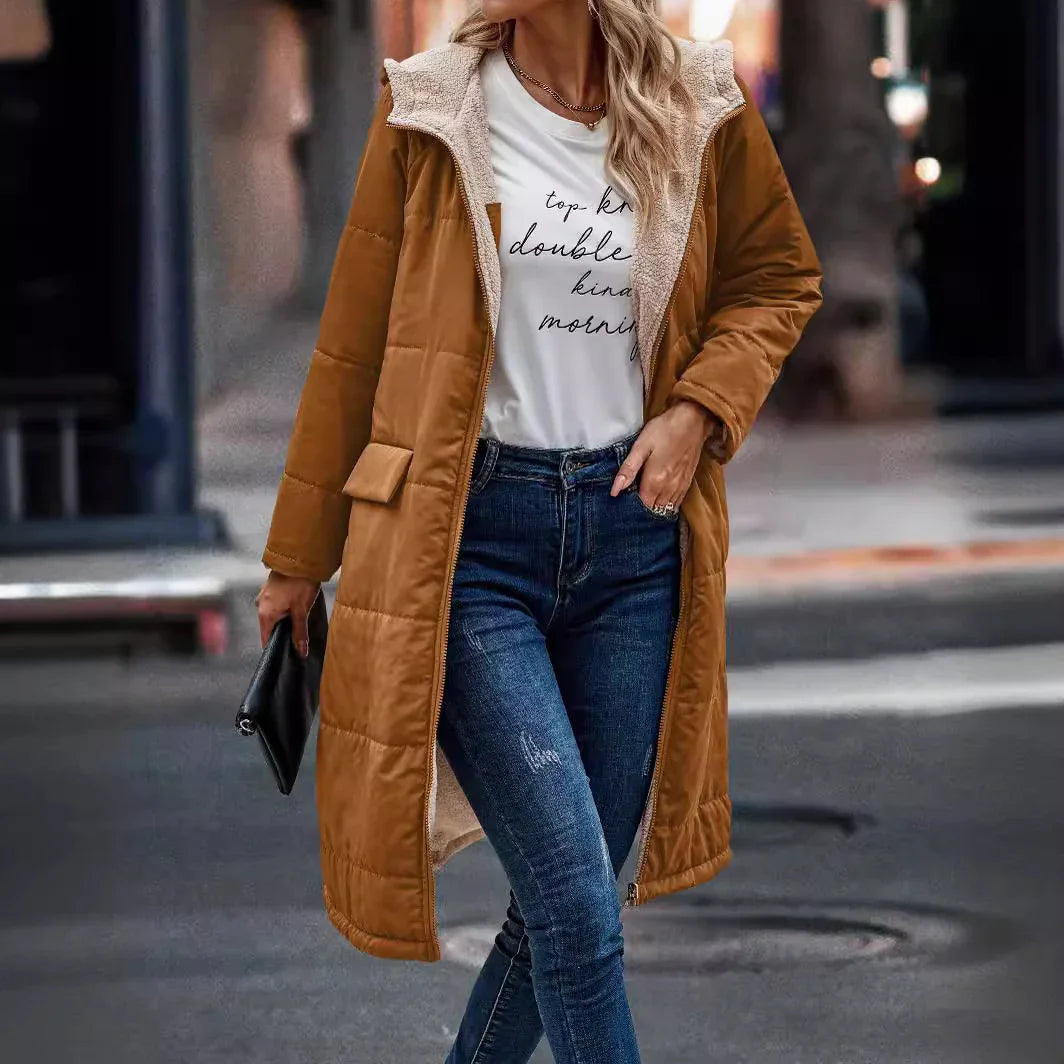 Woman wearing long brown padded winter coat with shearling lining, white graphic tee, and blue jeans walking in urban setting