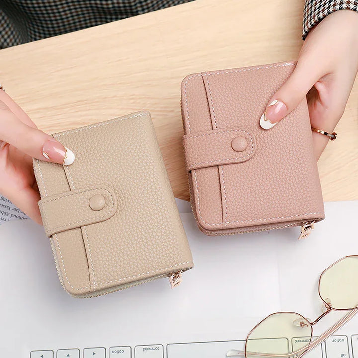 Two textured leather wallets in beige and dusty pink held by hands, with sunglasses and keyboard nearby