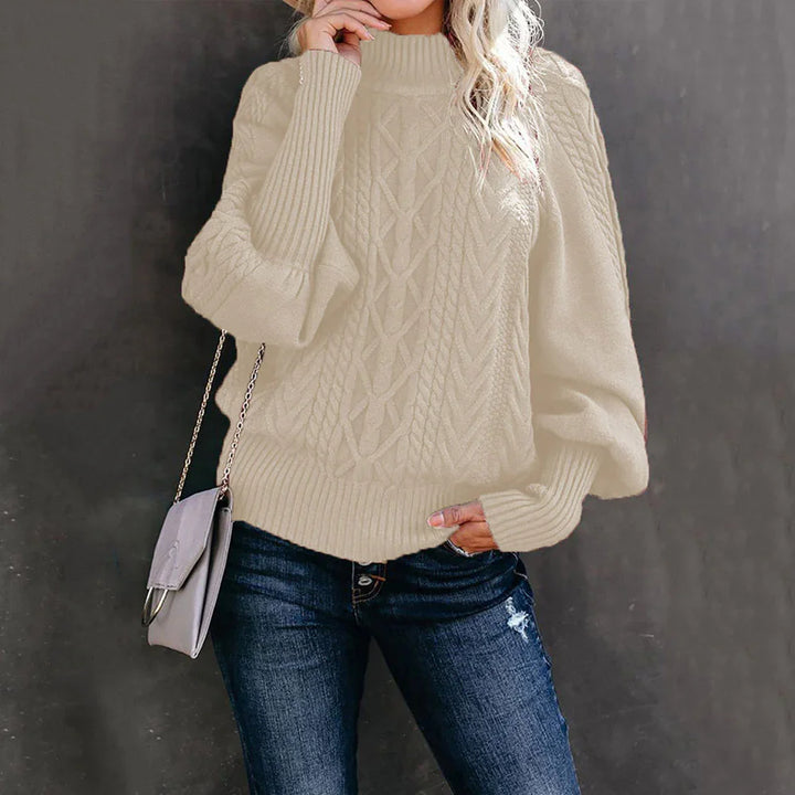 Woman wearing cream cable knit sweater with puff sleeves and dark blue jeans, holding gray chain purse