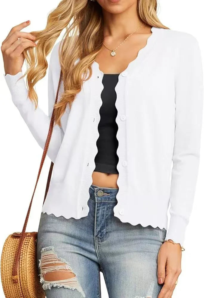 Woman wearing white scalloped buttoned cardigan over black top with ripped blue jeans and woven crossbody bag
