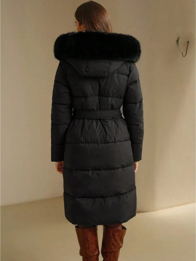 Woman wearing a black long quilted winter coat with a fur-trimmed hood and a belt, paired with brown boots
