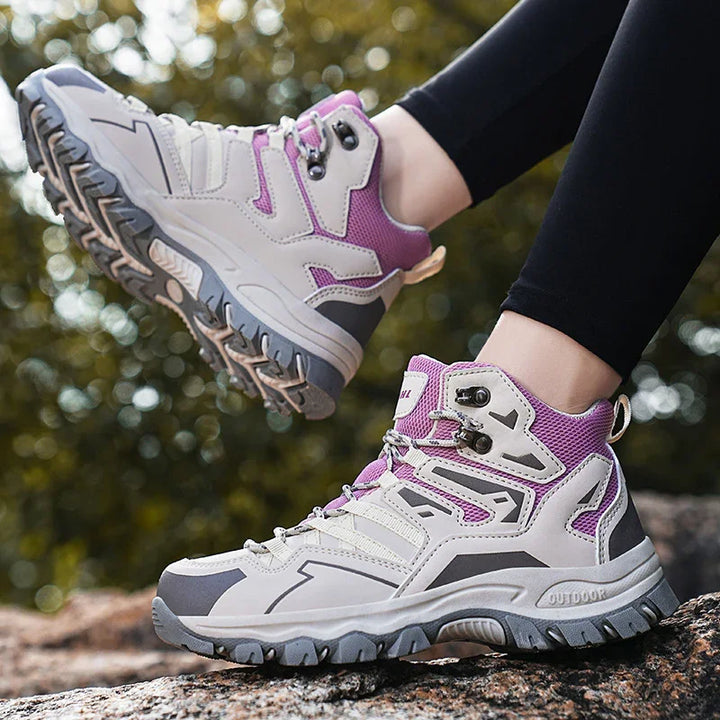 Light gray and purple outdoor hiking boots with rugged soles worn on black leggings outdoors