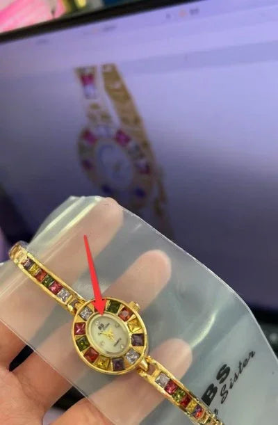 Gold bracelet watch with colorful square gemstones and small oval watch face held over a laptop screen