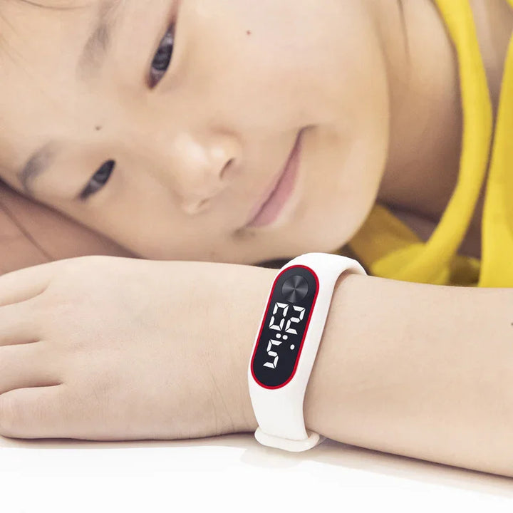 Child wearing white digital fitness tracker watch with black and red display showing time