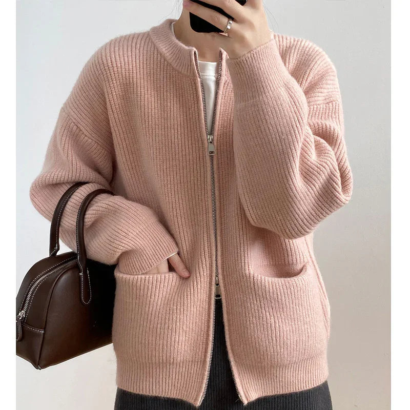 Person wearing a light pink ribbed zip-up cardigan with front pockets, holding a dark brown leather handbag.