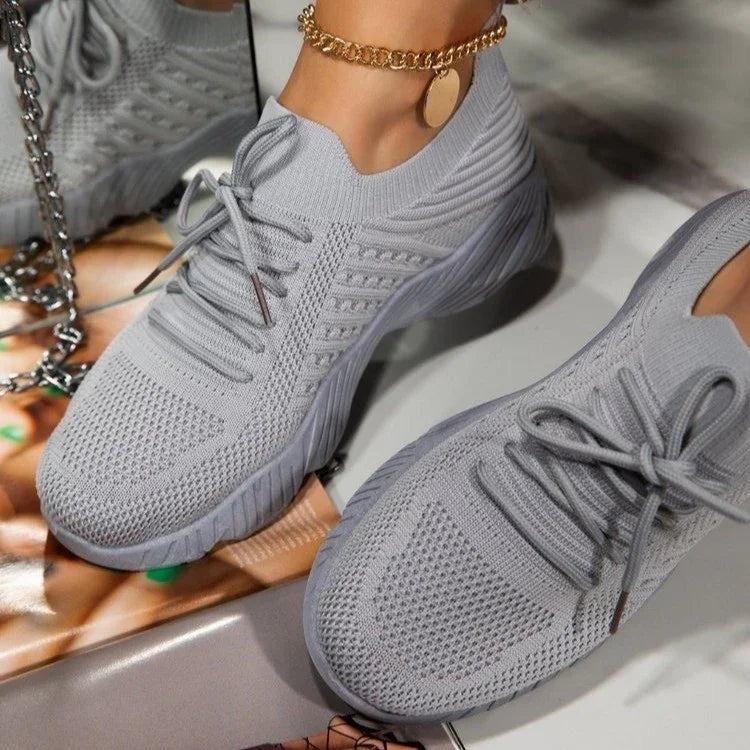 Close-up of light gray knitted sneakers with laces and a chunky sole, worn with a gold chain anklet