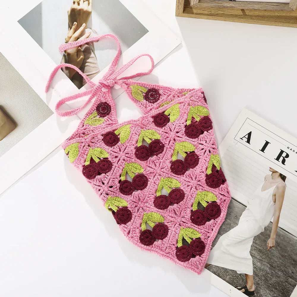 Pink crochet halter top with cherry patterns lying on white surface beside fashion magazines