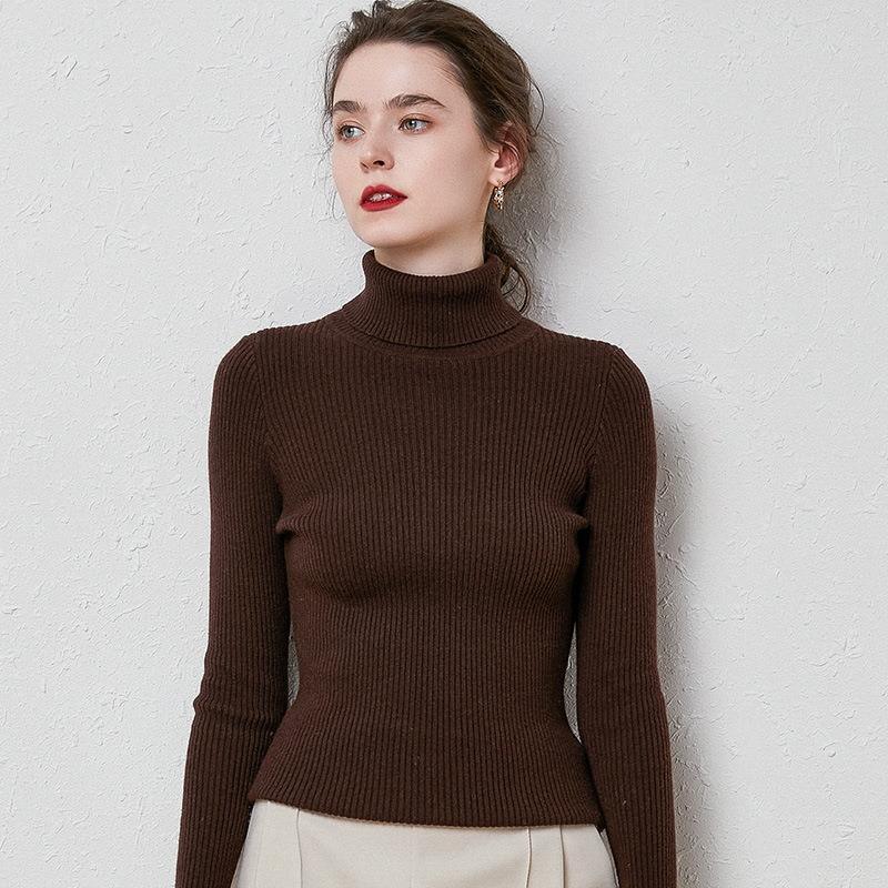 Woman wearing ribbed brown turtleneck sweater with long sleeves against textured white wall