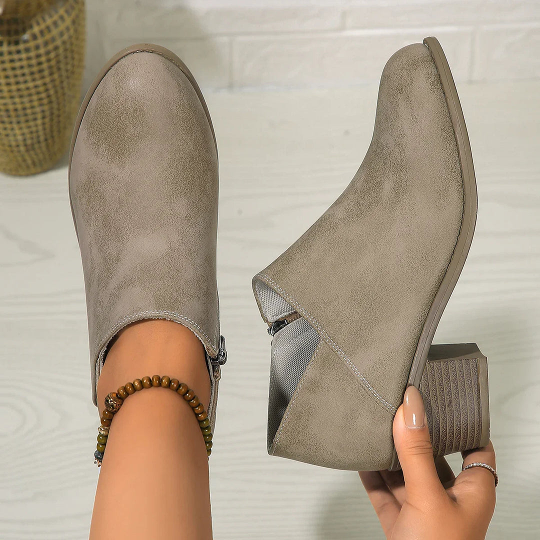 Taupe suede ankle boots with block heels and side zippers on light wooden floor