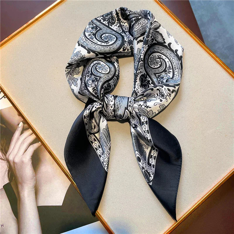 Black and white paisley silk scarf neatly tied on beige surface next to magazine