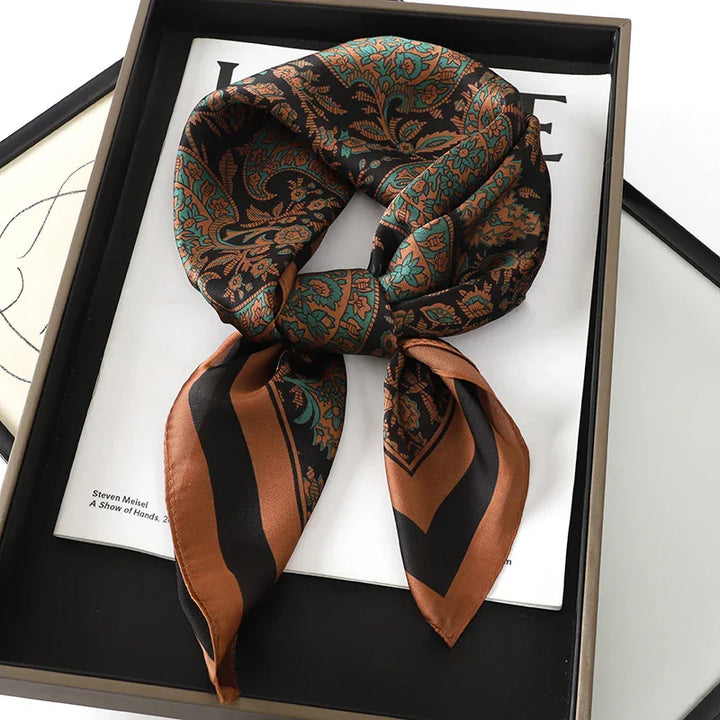 Silk scarf with intricate teal and brown paisley pattern, styled in a knot, on white paper in black box