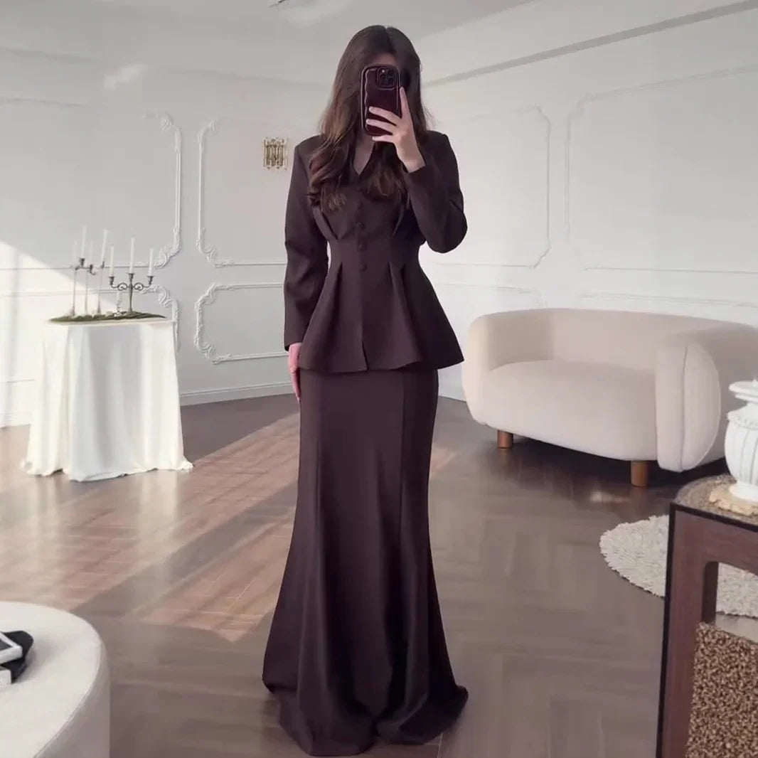 Woman in dark brown fitted blazer and mermaid skirt taking mirror selfie in elegant white room