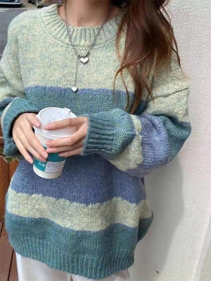 Person wearing a cozy striped wool sweater in blue, green, and beige holding a takeaway coffee cup