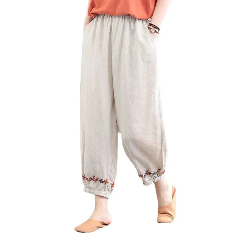 Beige loose linen pants with floral embroidery at ankles worn with orange top and tan slippers