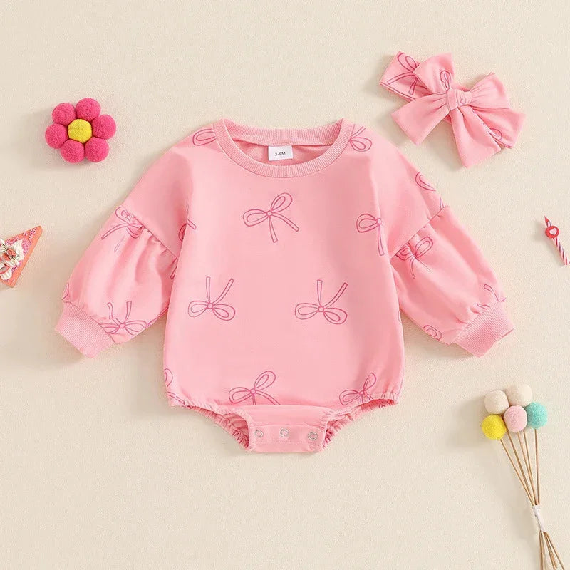 Pink long-sleeve baby romper with bow patterns and matching headband on beige background