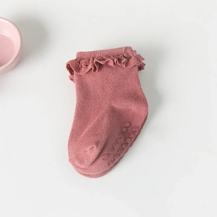 Pink baby sock with ruffled cuff and non-slip grip dots on white background
