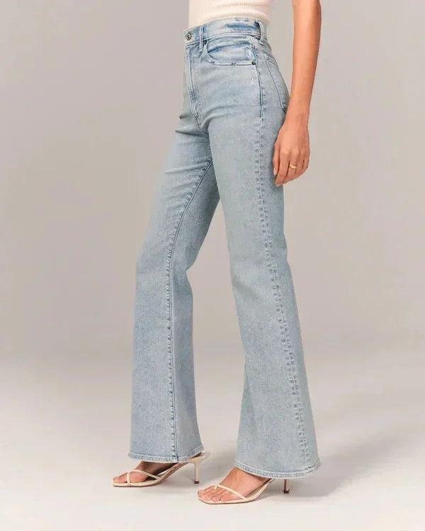 Woman wearing high-waisted light blue flare jeans with beige heeled sandals on neutral background