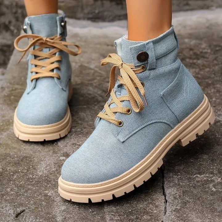 Light blue denim combat boots with beige laces and rugged beige soles on concrete ground