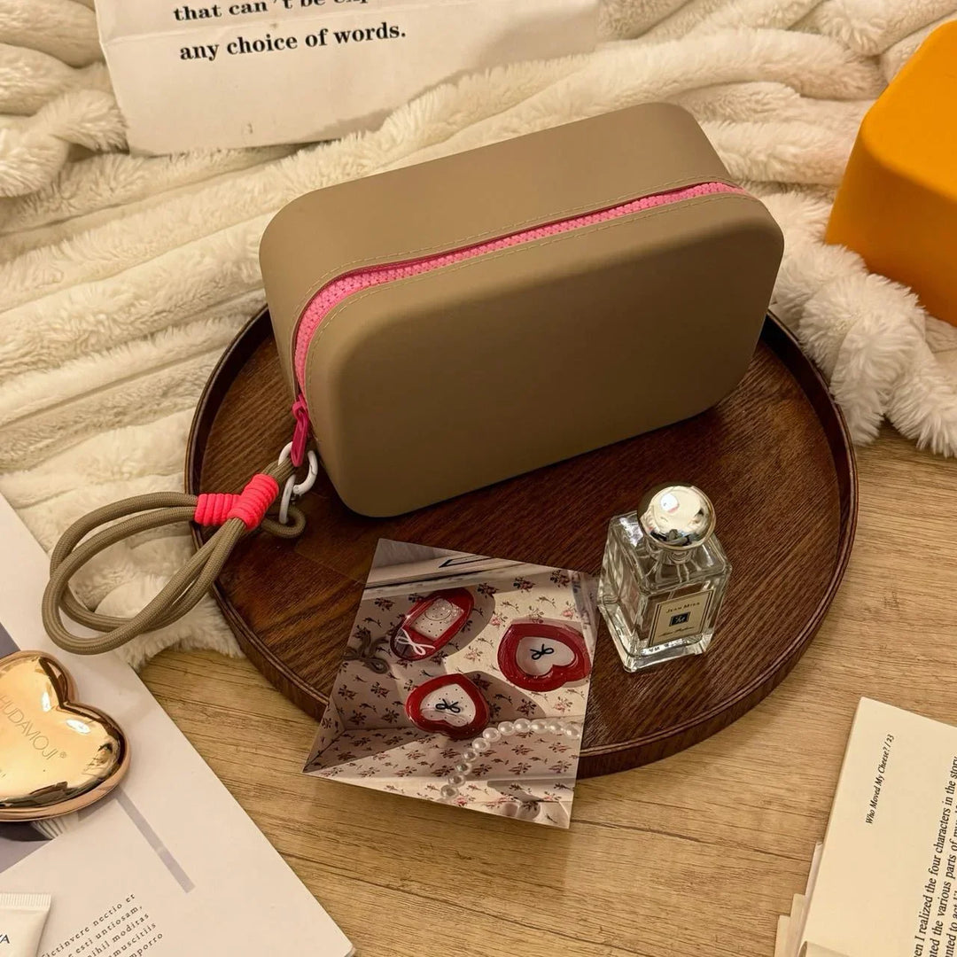 Brown rectangular pouch with pink zipper on wooden tray with perfume bottle and printed photo