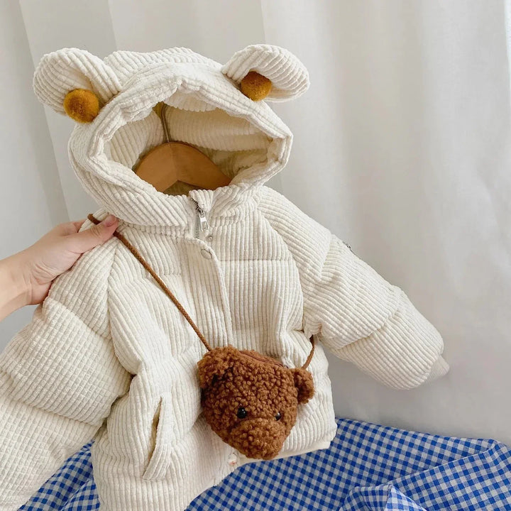 Cream-colored toddler corduroy winter jacket with hood and bear ears, paired with small brown teddy bear purse