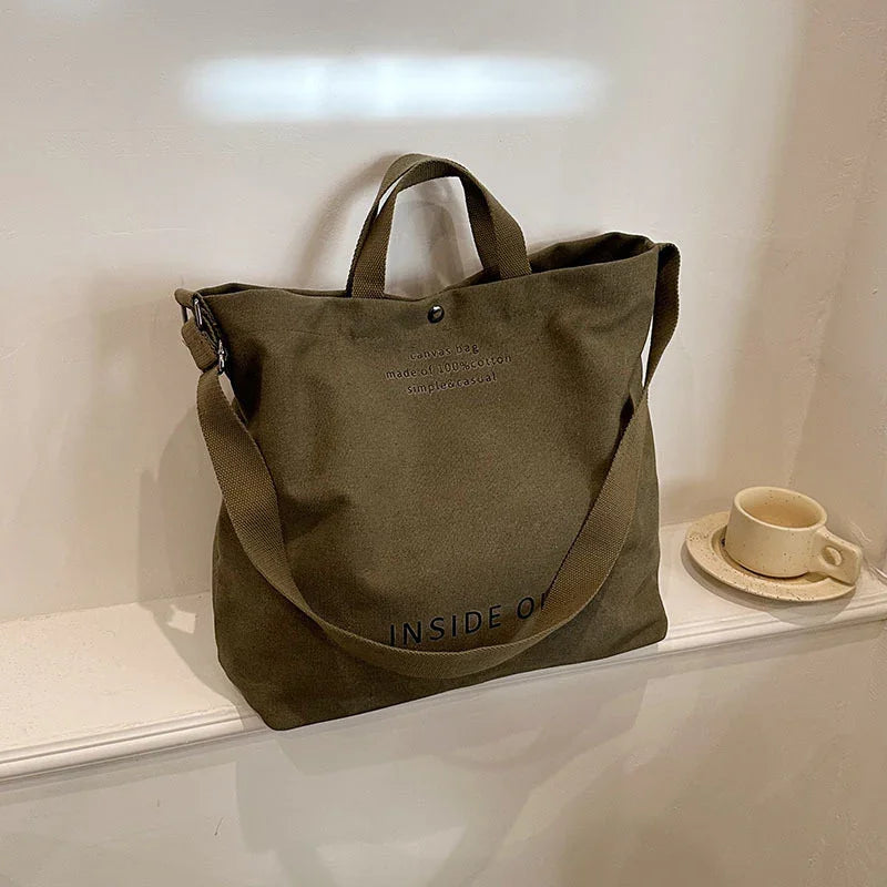 olive green canvas tote bag with handles and shoulder strap on white ledge next to ceramic cup and saucer
