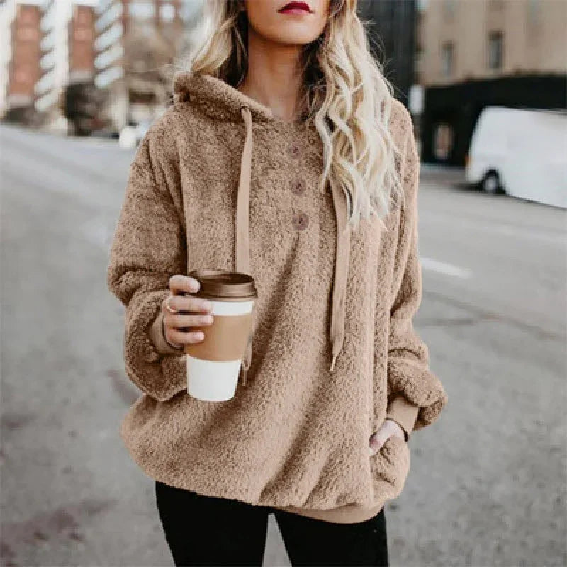 Woman wearing cozy brown sherpa hoodie holding a takeaway coffee cup on city street